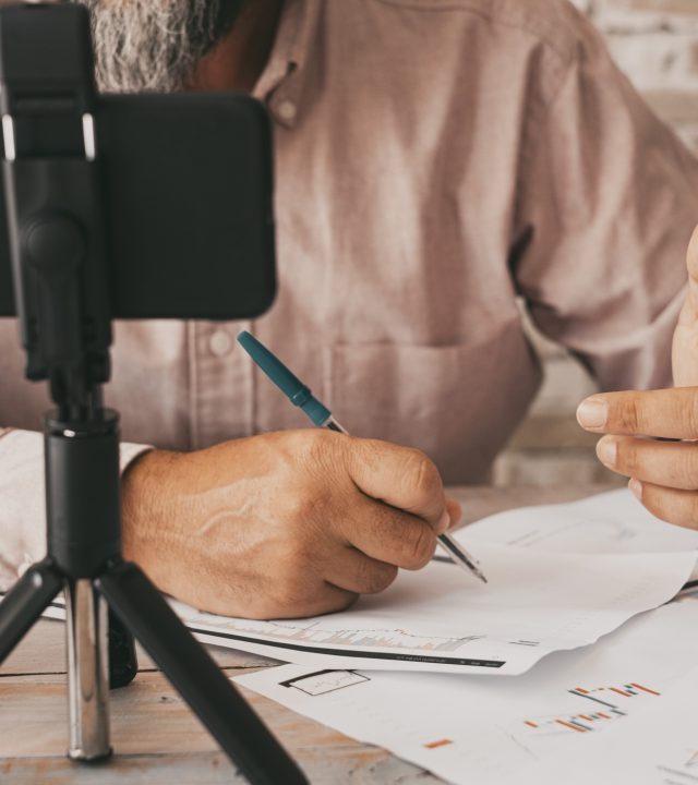 close up of people doing online contents using phone and little tripod. man writing on paper notes. concept of online job and contents creator working on the table. using mobile cellular for web